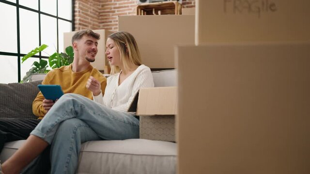 Young couple using touchpad sitting on sofa at new home