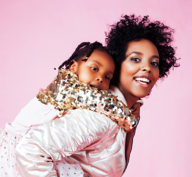 young pretty african-american mother with little cute daughter hugging, happy smiling on pink background, lifestyle modern people concept