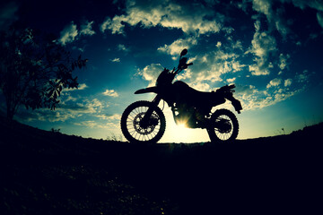 Silhouette of a motocross motorcycle parked on a mountain.