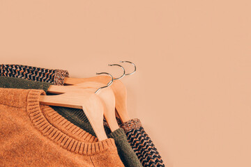 Wooden hangers with sweaters on beige background with copy space. Clothing donations, conscious and...