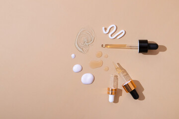 Smears and drops of various cosmetic products and a pipette on a beige background