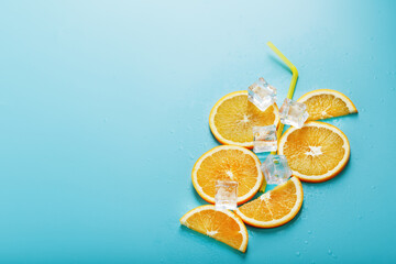 Orange slices and ice cubes with a straw on a blue background in the shape of a cocktail.