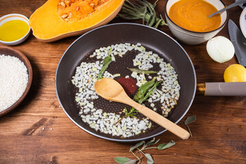 Making pumpkin risotto. Fried onions in a pan, raw rice, pumpkin and pumpkin puree nearby.