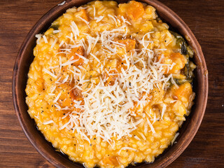 Portion of risotto with pumpkin and grated cheese on a plate, top view