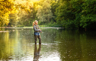 Fototapeta na wymiar A woman stands in the river and fishes with a spinning rod