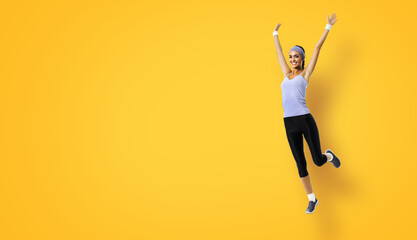 Fototapeta na wymiar Full body of joyful young woman jumping or doing fitness exercise, isolated over yellow background. Fit girl with raised up hands, in grey sportswear, at studio shot.
