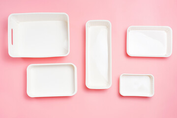 Plastic boxes of different sizes for storing clothes on a pink background, top view close up.