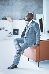 Secured Successful Businessman in Stylish Formal Suit Sits on the Back of the Sofa Cross-legged in...