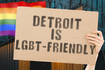 The phrase " Detroit is LGBT-Friendly " on a banner in men's hand with blurred LGBT flag on the background. Human relationships. different. Diverse. liberty. Sexuality. Social issues. Society