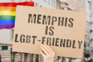 The phrase " Memphis is LGBT-Friendly " on a banner in men's hand with blurred LGBT flag on the background. Human relationships. different. Diverse. liberty. Sexuality. Social issues. Society