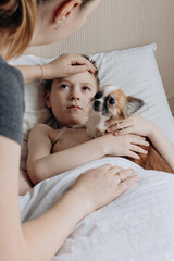 Sick boy with thermometer laying in bed and mother hand taking temperature. Mother checking temperature of her sick son who has thermometer. Sick child with fever and illness in bed.