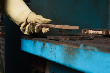 Cropped view of welder in protective glove holding brush above detail in factory