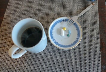 refeição. Prato com comprimidos e uma chávena de café negro.