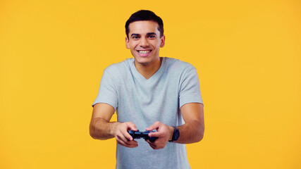 KYIV, UKRAINE - DECEMBER 22, 2021: joyful young man holding joystick and playing video game isolated on yellow.