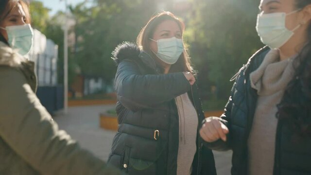 Mother and daughters wearing medical mask standing bump elbow at park