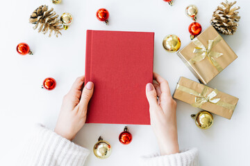 a red book in the hands of a young girl against the background of gifts and Christmas toys. the...
