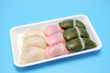 Korean traditional rice snack tteok in a plastic plate on blue background, close-up.