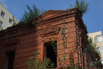 An old brick building built in the 19th century is overgrown with trees in the city center.