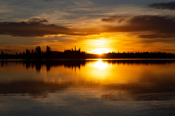 Orange sunset over lake with black silhouette tree line and clouds in the sky
