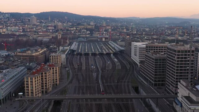 Aerial drone footage with a forward motion of a train reaching the Zurich Hauptbahnhof, the central train station, in Switzerland largest city at sunset. 