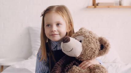 Smiling kid hugging teddy bear in bedroom.