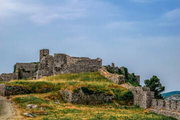 Fototapeta na wymiar Stone ruins of Shkoder Castle among the green-yellow summer lawn. Remains of a medieval fortress isolated on blue sky background