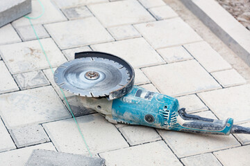 A worn-out diamond angle grinder lies on the paving slabs in front of the work area. Copy space.