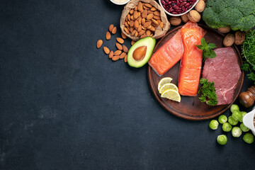 Green vegetables, nuts, beans with beef meat and salmon fish on dark background with copy space top view. Raw healthy food, clean eating or balanced diet concept