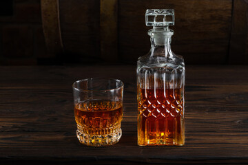 Glass decanter with cognac, brandy on a vintage background of a rustic oaken barrel. Alcoholic beverage. Still life in the old style