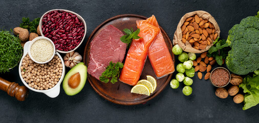Set of green vegetables, nuts, beans, microgreen with beef meat and salmon fish on dark background top view. Raw healthy food, clean eating or balanced diet concept
