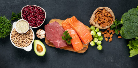 Set of green vegetables, nuts, beans, microgreen with beef meat and salmon fish on dark background...