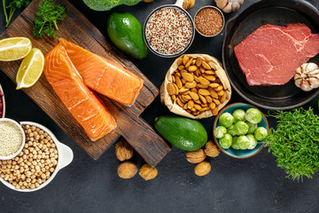 Set of green vegetables, nuts, beans, microgreen with beef meat and salmon fish on dark background with copy space top view. Raw healthy food, clean eating or balanced diet concept