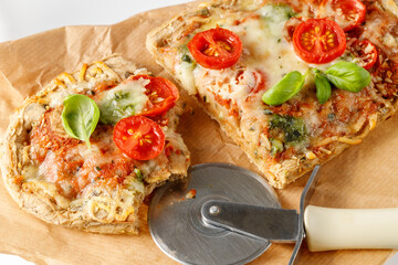 Cut and bitten small oval pizza baked from dark rustic wheat rye dough with cherry tomatoes,...