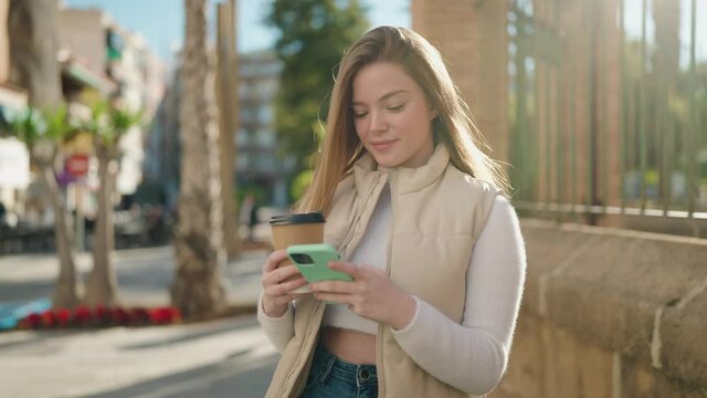 Young blonde woman using smartphone drinking coffee at street