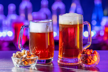 Glass of beer on bar counter. Jugs, mugs, pints of brew beverage, ale, cider on wooden table in pub, bar. Backlit dark showcase with craft beer bottles in brewery. French fries fried potatoes snack