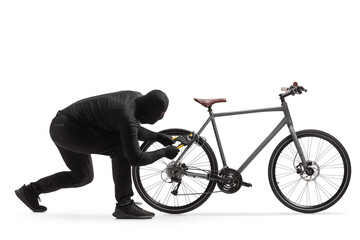 Burglar in black clothes with a balaclava cutting the lock chain of a bicycle