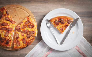 Slice of pizza on plate, fork, knife on wooden table. Pizza on circle board