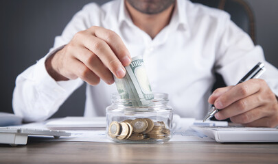 Businessman putting money in glass bank. Saving money