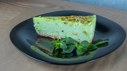 Close-up view of green pistachio cake with leaf of mint on black plate. Creamy pistachio cheesecake.