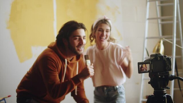 Young couple dancing while making overhaul, recording video about renovating and painting walls together. Man and woman making vlog about interior design, new apartment, having fun.