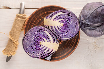Two half of fresh red cabbage with a clay plate and a knife on a wooden table, close-up, top view.