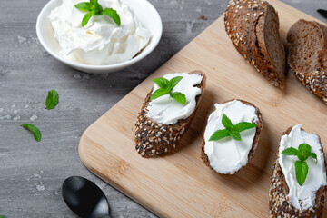 Home made bread on a wooden cutting board with curd cheese and ricotta and herbs. Decorated with min