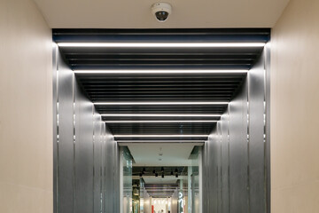 A narrow corridor of the restaurant with lighting and metal walls. Mirrored metal surface reflecting light from the diode backlight