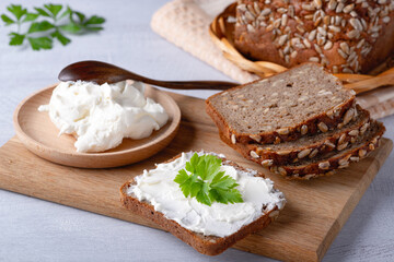 Fototapeta na wymiar Rye bread on a wooden cutting board with curd cheese and ricotta and herbs. Decorated with green herbs