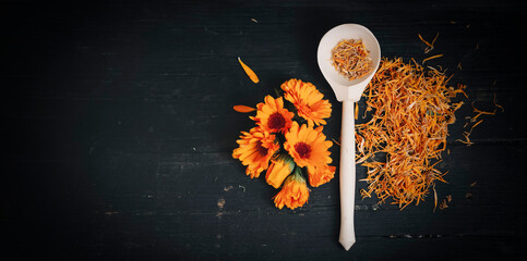 bright fresh flowers and dried calendula flowers on a black wooden background top view with a copy of the space.