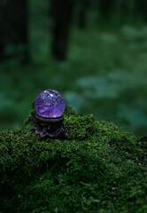 Amethyst crystal ball in forest, natural dark green background. Magic quartz ball for healing Crystal Ritual, Witchcraft, spiritual esoteric practice. Reiki life balance concept