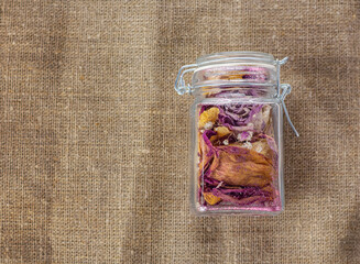 glass jar with bright dried flowers and petals on a burlap background
