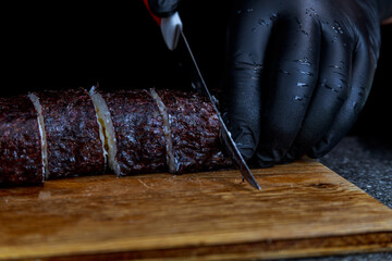 A sushi roll, wrapped in nori, a chef in black gloves cuts with a knife on a wooden board