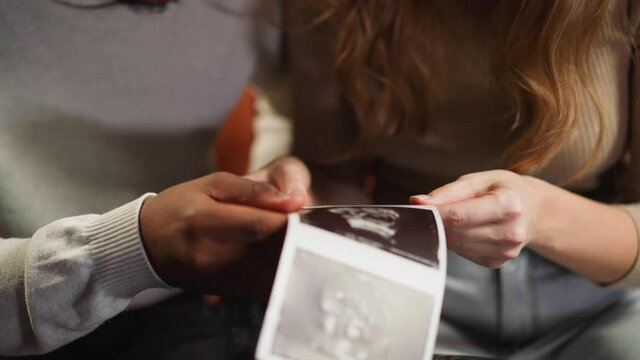 Young couple holds ultrasound pictures of baby in room