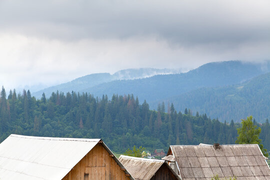 Roofs of village houses on the background of spruce forest and mountains in fog. Ukraine, carpathians.